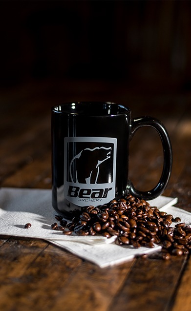 Bear Archery coffee mug on table with coffee beans surrounding